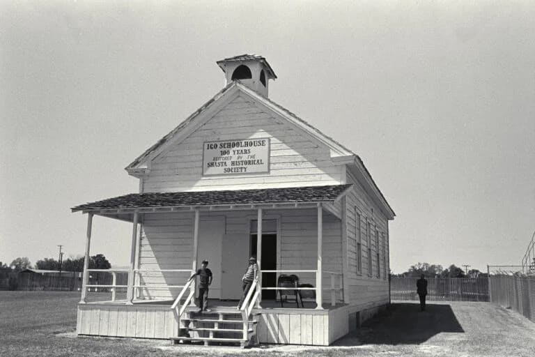 Historic one-room schoolhouse with "100 Years" commemorative sign, featuring a front porch and bell tower.