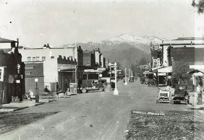 Street scene with buildings, vehicles, and snow-capped mountains in the background.