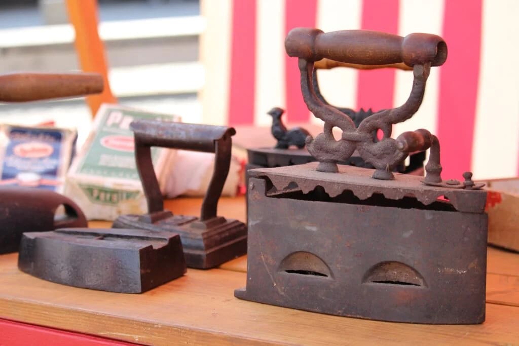 Antique cast iron flat irons with wooden handles displayed on wooden surface.