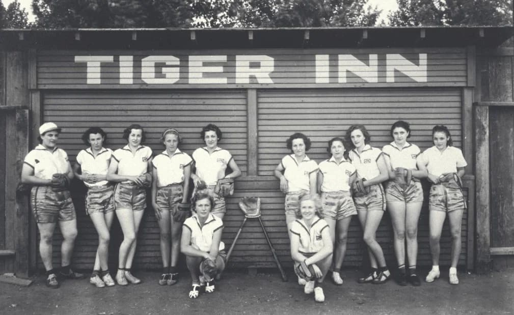 Twelve women in athletic uniforms pose before a "Tiger Inn" building, circa mid-20th century.
