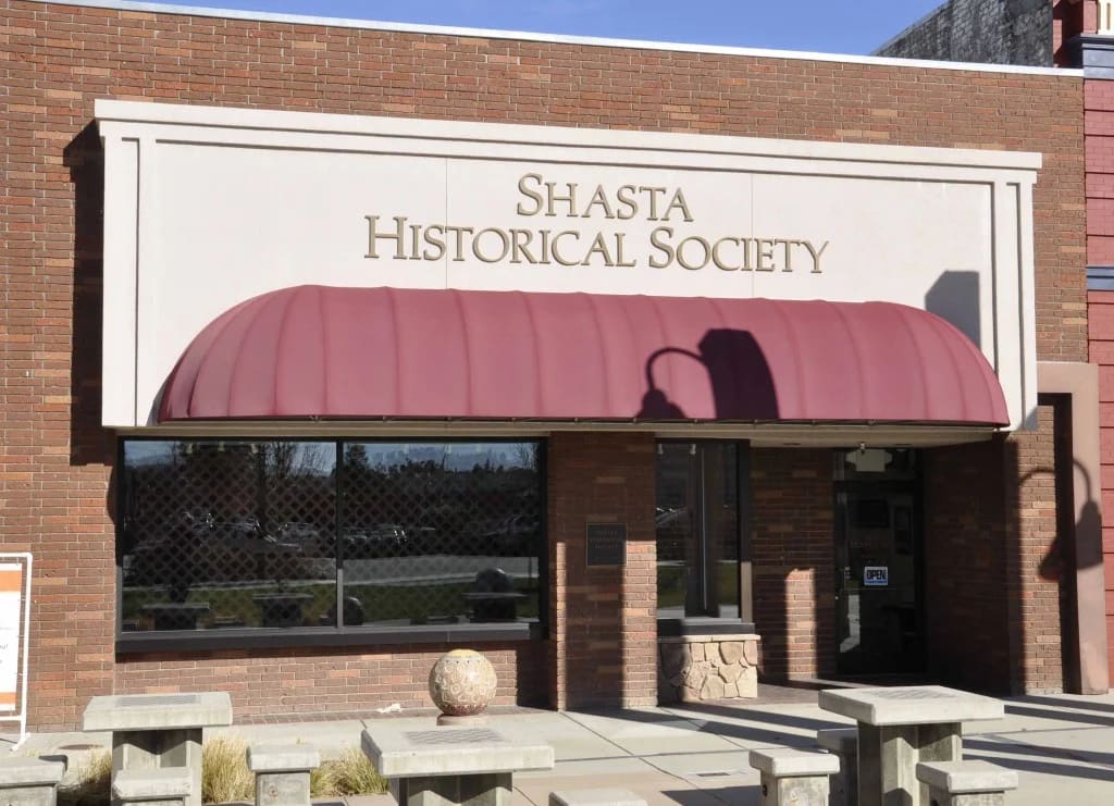 Storefront with "Shasta Historical Society" sign and burgundy awning on brick building.